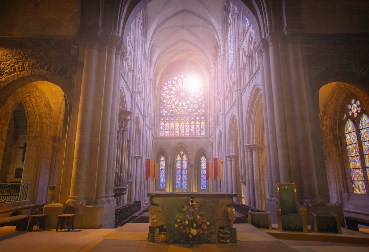 Sunlight streams through elaborate stained glass in a vast Saint-Vincent cathedral interior with towering arches, Saint-Malo, Bretagne, France