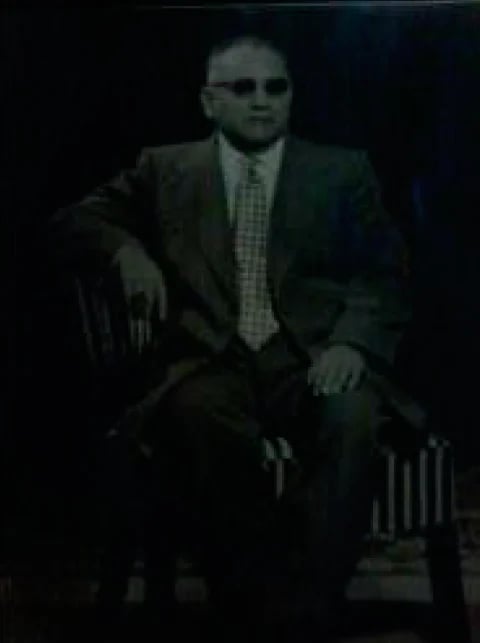 Hombre de traje oscuro y lentes sentado en un ambiente de penumbra
