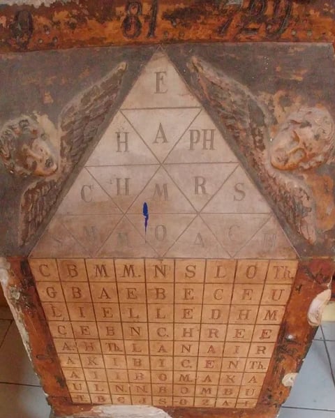 Ancient frieze showing a triangular alphabet grid with winged figures on sides and letter squares below