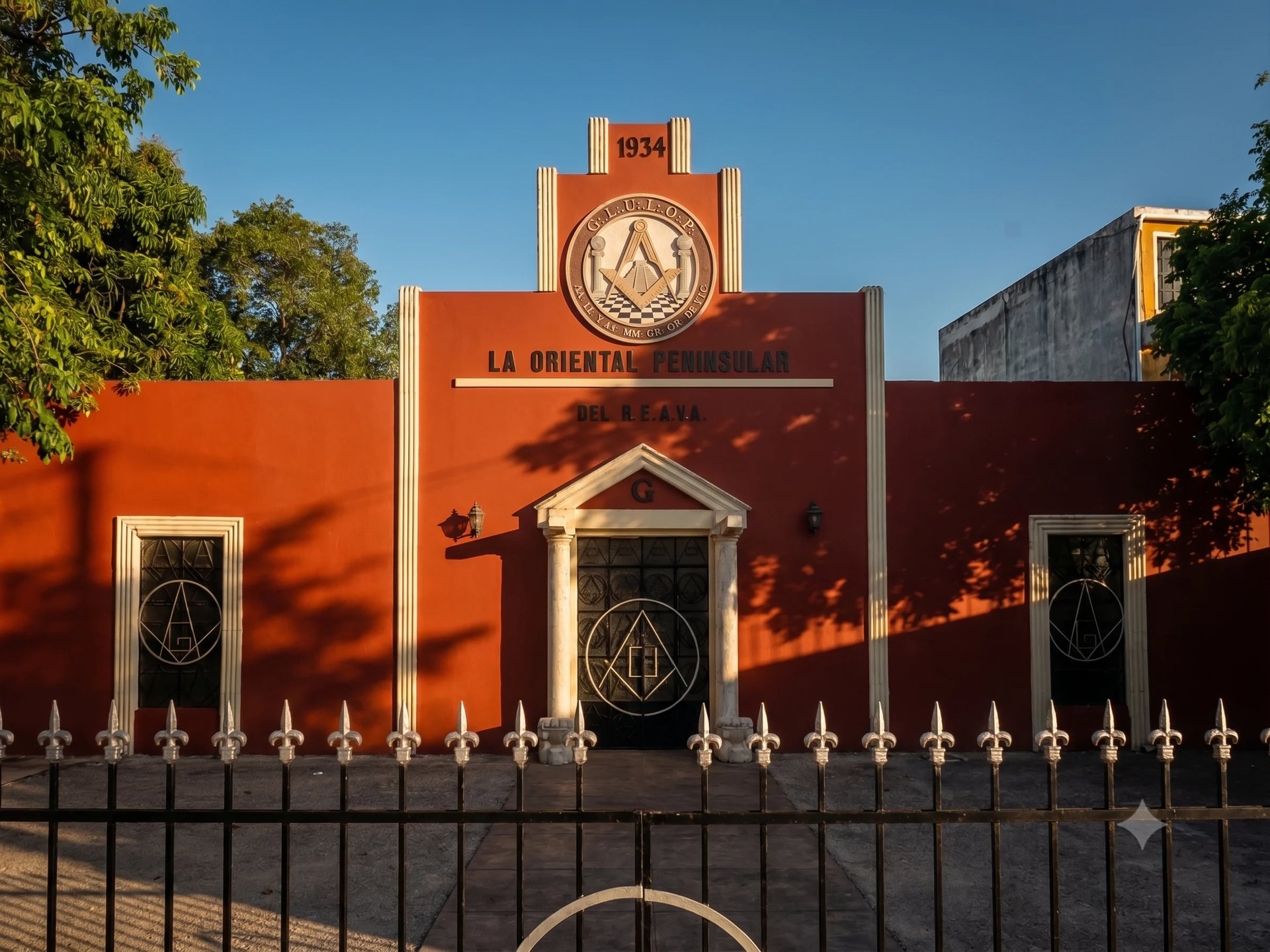 Templo masónico de la calle 63 en el centro de Mérida, edificio naranja con letrero La Oriente y torre con reloj, con diseños geométricos en las puertas y reja blanca
