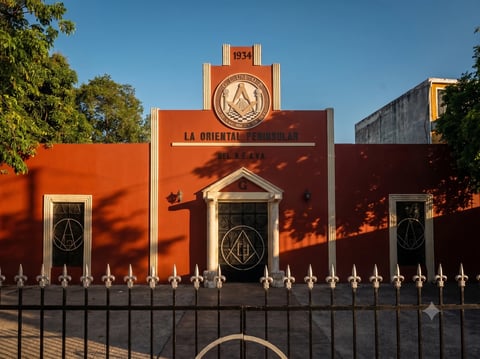 Templo masónico de la calle 63 en el centro de Mérida, edificio naranja con letrero La Oriente y torre con reloj, con diseños geométricos en las puertas y reja blanca